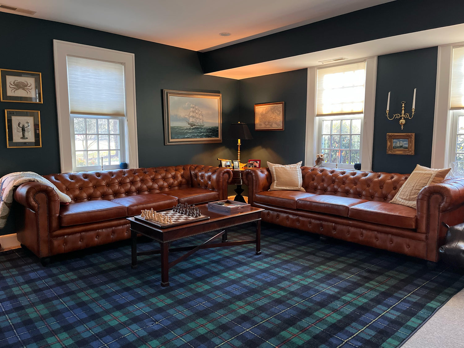 Two three seater, buffalo brown Chesterfield leather sofas in an elegant New England inn, with navy blue walls and nautical paintings on the wall.